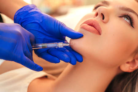 Beautiful woman gets an injection in her face. she has fashion make up and red shining lips