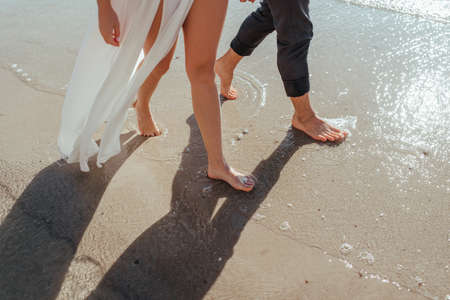 feet of couple. Woman and man in the sea waves on sunsetの写真素材