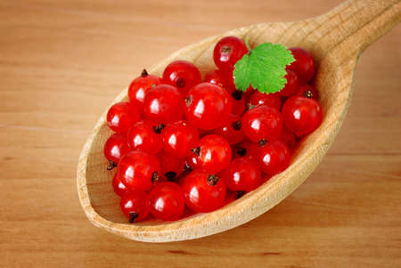 currant berries with green leaf in wooden spoonの写真素材