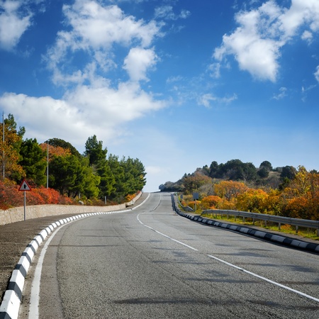 wide empty road between autumn trees and blue cloudy skyの写真素材