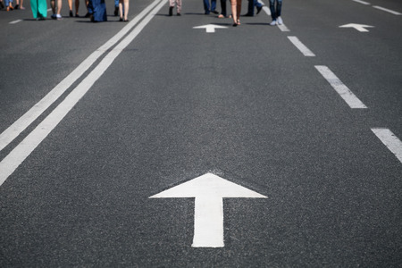 direction arrow on city asphalt road and walking people, selective focus on foreground