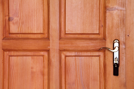 brown wooden door with handle and key in keyhole closeupの写真素材