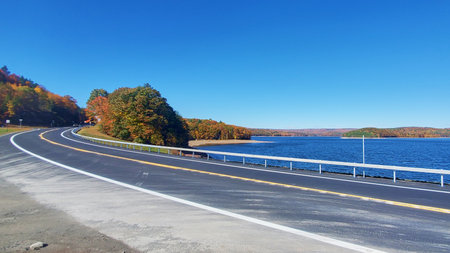 Photograph of a road surrounded by beautiful autumn forest by a lake in the USAの写真素材