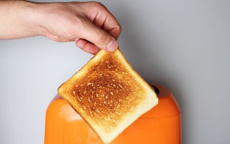 hand toast and orange toaster on a light backgroundの写真素材