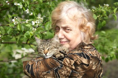 The old woman holds on hands cat against a blossoming treeの写真素材