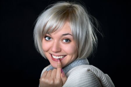 The smiling girl holds a finger at  mouth on  black backgroundの写真素材