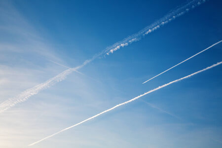 Airplane with trail against the blue skyの写真素材