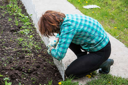 Woman fixing a decorative fence on a flower bedの写真素材