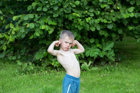 little boy shows biceps in the garden on a summer dayの写真素材