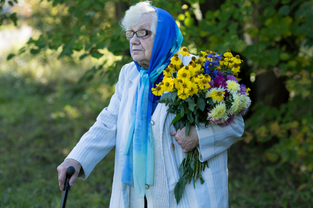 grandmother with a cane and flowers on the background of treesの写真素材