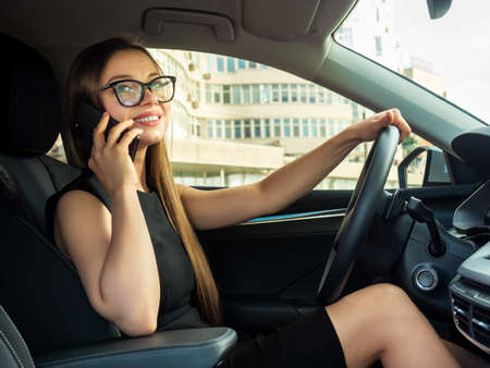 Modern beautiful woman businesswoman with glasses peeks out of her car.の写真素材