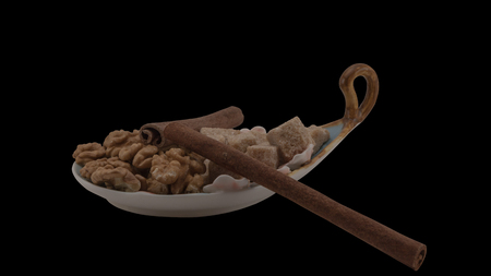 The saucer in the shape of a boat, filled with walnuts and cane sugar, and the cinnamon sticks that look like oars. The still life is isolated on a black background.の写真素材