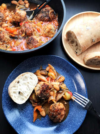stewed meatballs with vegetables in a frying pan and in a plate on the tableの写真素材