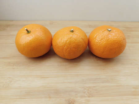 Three fresh tangerines lie on a wooden background.の写真素材