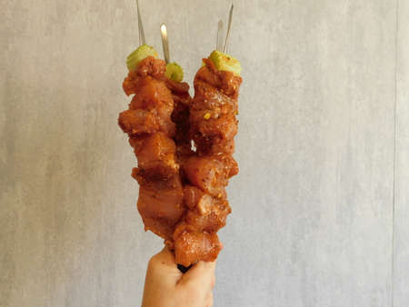 Hands are holding barbecue made from pork and vegetables on metal skewersの写真素材