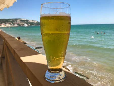 a glass of light beer in a womans hand in a restaurant on the background of the sea. Balchik. Bulgaria.の写真素材