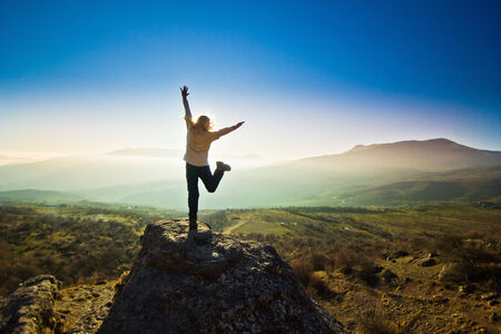 freedom girl with hands up in the mountains against sunの写真素材