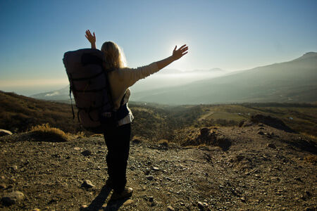 freedom girl with backpack and hands up in the mountains against sunの写真素材