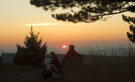 young couple sitting at sunset in mountainsの写真素材
