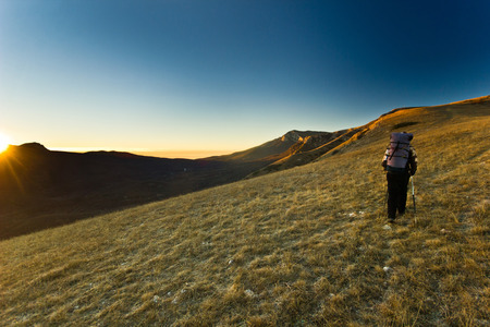 lonely girl with backpack in the mountains on a hill at sunrise