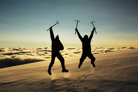 jumping two man on a snowy slope in the mountains against sun at sunriseの写真素材