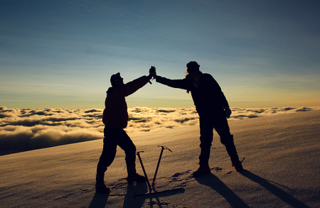 standing two man on a snowy slope in the mountains against sun at sunrise