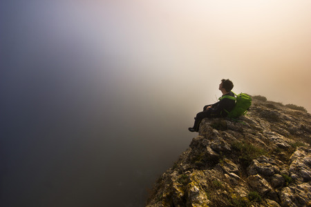 man sitting on top of a cliff in foggy weatherの写真素材