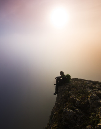 man sitting on top of a cliff in foggy weatherの写真素材