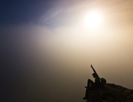 man sitting hands-up on top of a cliff in foggy weatherの写真素材