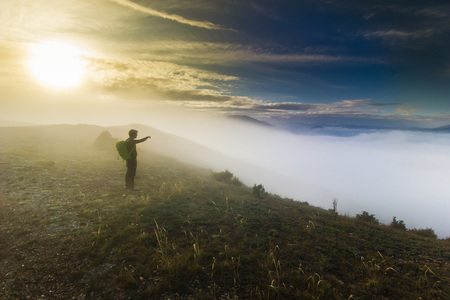 man with backpack standing on a hill in foggy weatherの写真素材