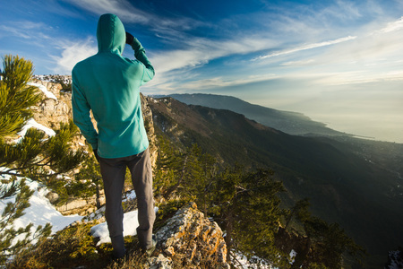 man  standing on a cliff in mountains at sunrise and looking on seaの写真素材