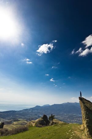 man on the cliff with hands up in mountains with blue skyの写真素材