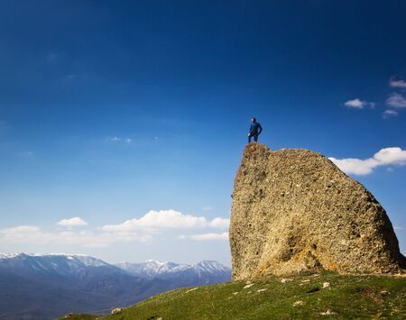 man on the cliff with hands up in mountains with blue skyの写真素材