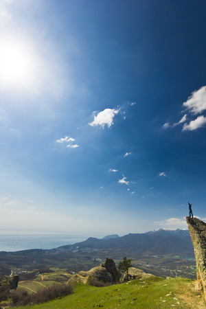 man on the cliff in mountains hands-up with blue sky and green grassの写真素材