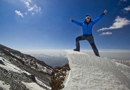 happy man in blue jacket with hands-up standing on a cliff in mountains at sunriseの写真素材