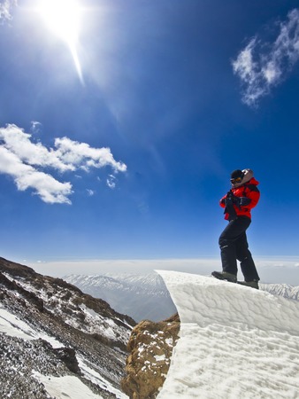 happy man in red jacket with hands-up standing on a cliff in mountains at sunriseの写真素材
