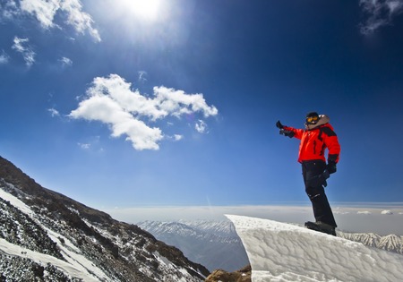 happy man in red jacket with hands-up standing on a cliff in mountains at sunriseの写真素材