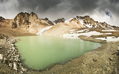 blue mountain lake surrounded by high snowy peaks reflects rocksの写真素材
