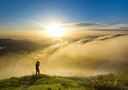 man with camera making photo on a hill at sunset and clouded skyの写真素材