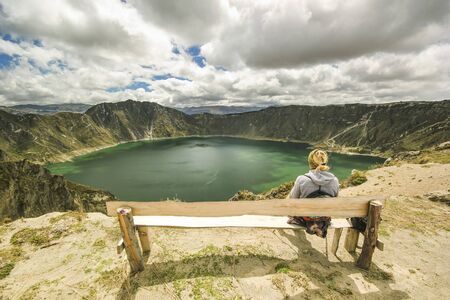 girl sitting on a branch above crater lake in ecuador with clouds on skyの写真素材
