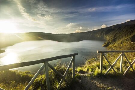 fence and crater lake in sunset in ecuador against sunの写真素材