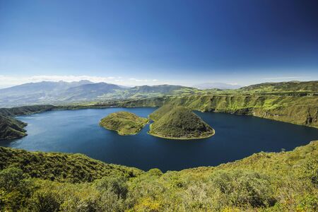 blue volcanic crater lake with two islands at daylight in ecuadorの写真素材
