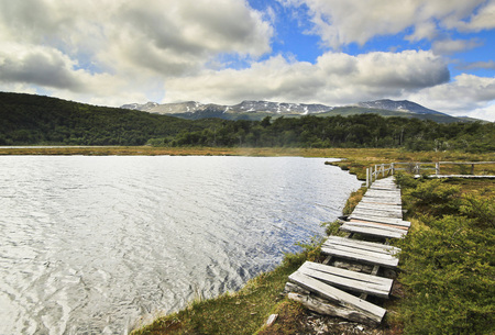 lake with wooden walkway on shore with moutains on background and sky with cloudsの写真素材
