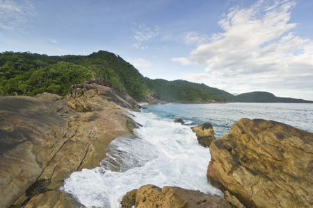 beautiful tropical beach with blue pure water waves, stones and green mountainsの写真素材
