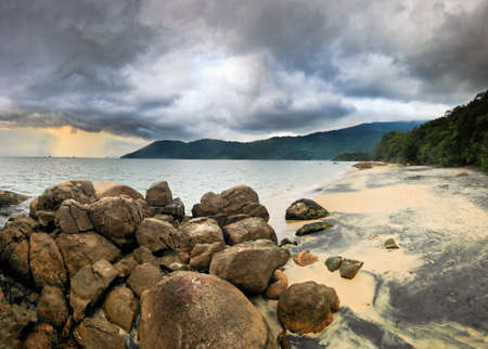 sunset with big clouds in tropical beach with water waves, sand and stones on shoreの写真素材