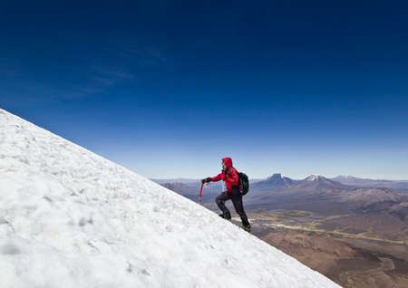 man in red jacket with ice-axe and backpack climbing on glacier of Sajama Volcano in Boliviaの写真素材