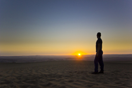 standing man at sunset in desert with shining sunの写真素材