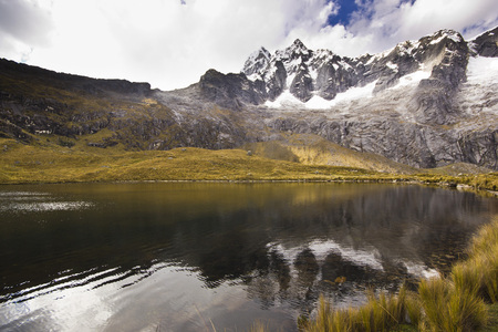 dark lake in foot of snow-covered mountain in Peru with steep slopes at sunriseの写真素材