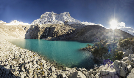 blue lake in foot of snow-covered mountain in Peru with steep slopes at sunriseの写真素材
