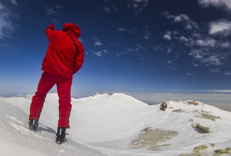 man standing on a cliff in mountains with snowy picks and blue sky with clouds on backgroundの写真素材